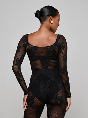 A woman with her hair in a bun is shown from the back, wearing the L'AGENCE Gwendolyn Mesh Knit Bodysuit with floral lace details and matching high-waisted bottoms, standing against a plain gray background.
