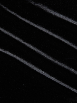 The Seraphine Velvet Bodysuit by L'AGENCE features black stretch velvet with soft, diagonal folds, creating subtle lines and highlights for a smooth, plush texture and a luxurious look.