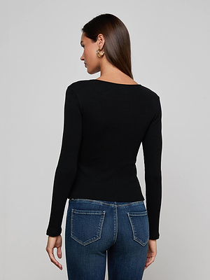 A woman with straight brown hair, in a L'AGENCE Scarlet Scoopneck Tee and blue jeans, stands facing away from the camera against a plain light background.