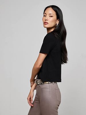 A woman with long dark hair poses in the Stormy Cropped Cotton Tee, paired with taupe pants and a snakeskin belt, looking confidently at the camera against a plain light background.