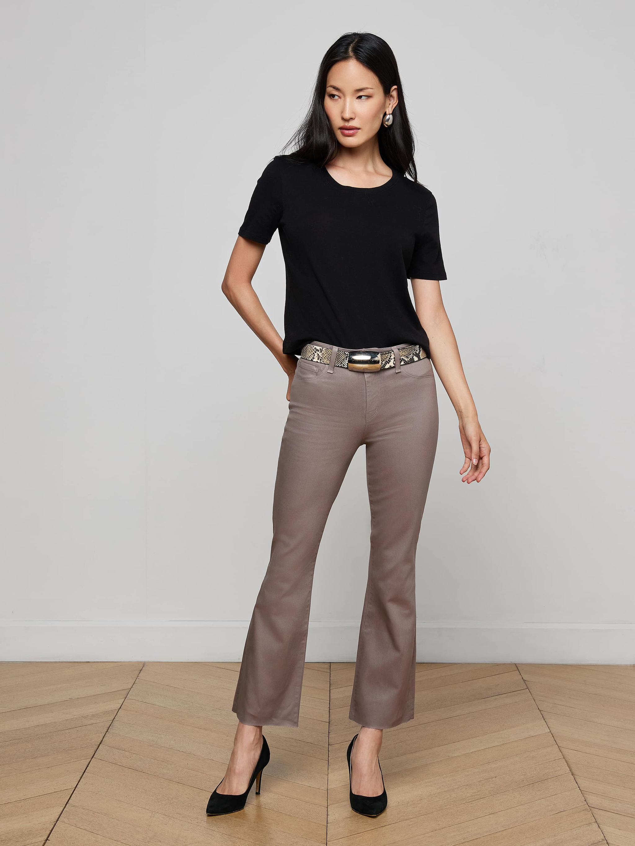 A woman wearing the Stormy Cropped Cotton Tee in black, paired with sunglasses, white pants, and black heels stands against a plain white background.