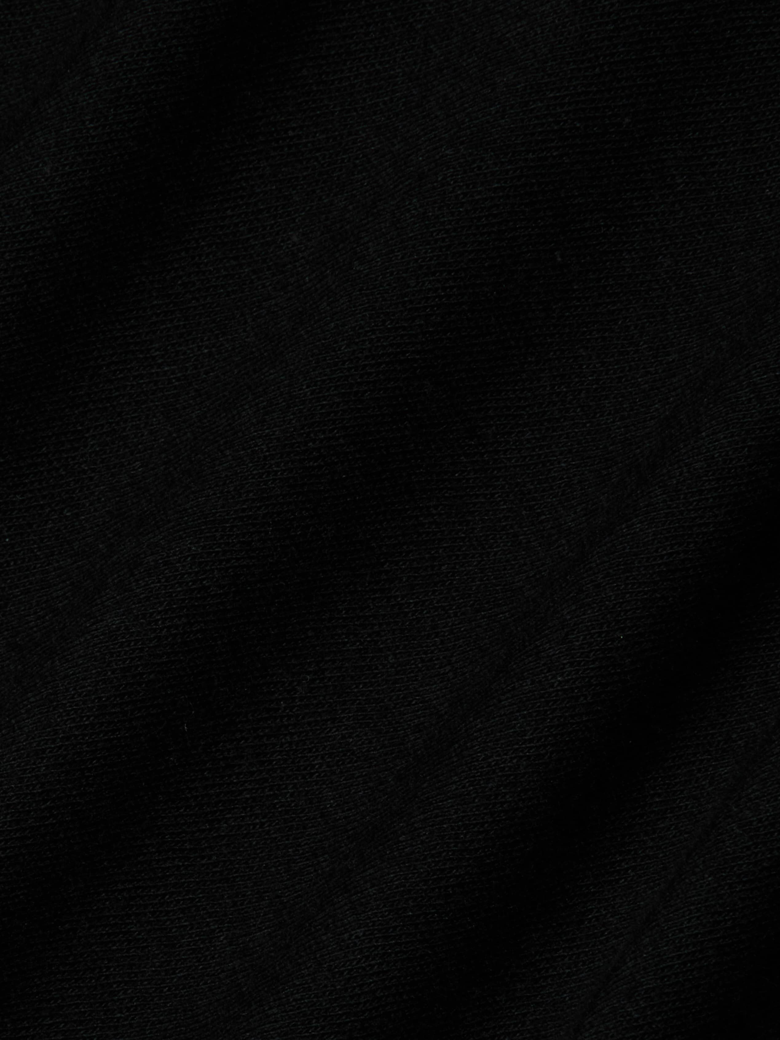 Close-up of black fabric with a subtle diagonal weave pattern visible in the texture, characteristic of the Stormy Cropped Cotton Tee crafted from organic cotton in a semi-relaxed fit.