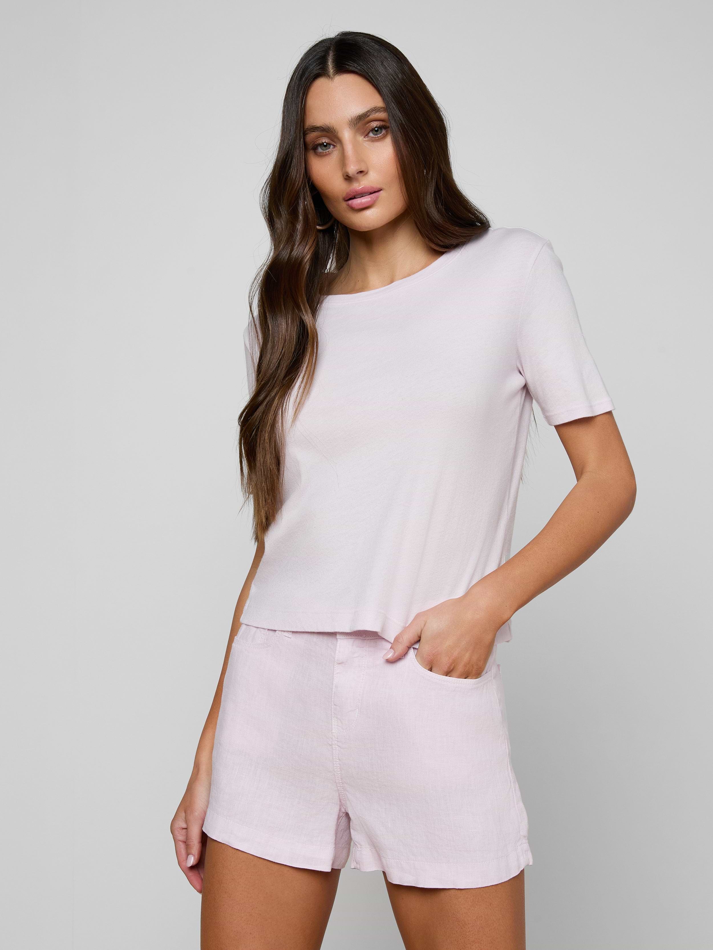 A woman with long brown hair wears the Stormy Cropped Cotton Tee in light pink—a semi-relaxed fit, cropped t-shirt—paired with matching shorts, standing with one hand in her pocket against a plain background.