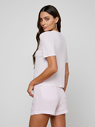 A woman with long brown hair wears the Stormy Cropped Cotton Tee in light pink paired with matching shorts, standing against a plain light background and looking over her shoulder with one hand on her hip.