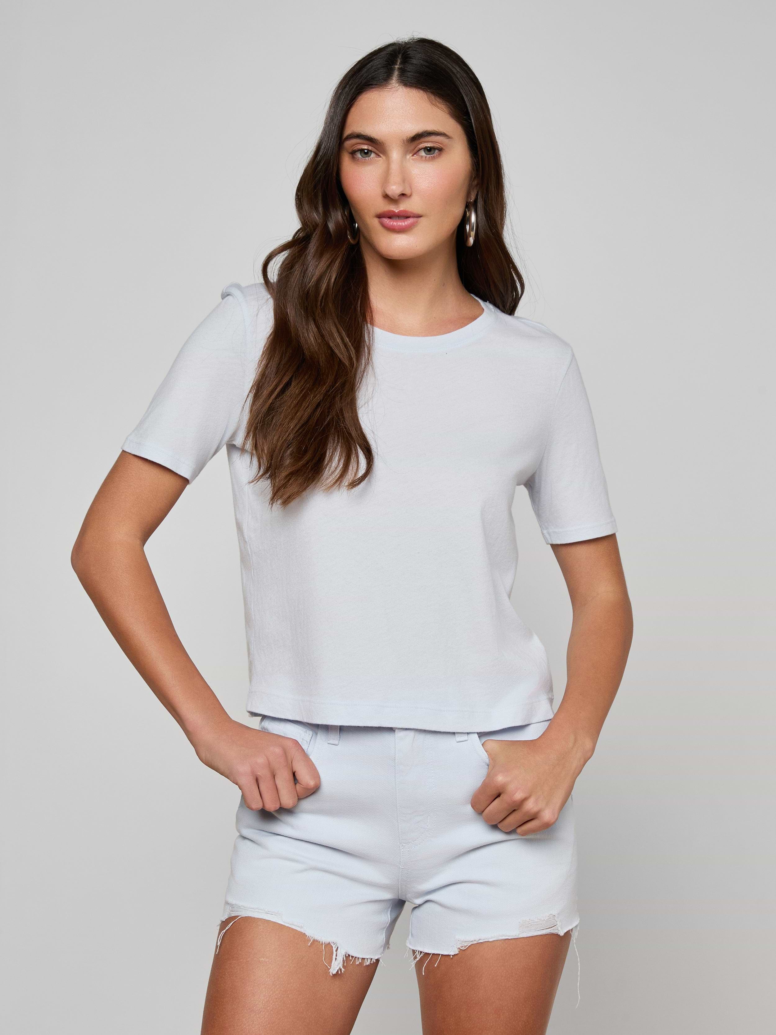Wearing the Stormy Cropped Cotton Tee—a semi-relaxed fit top crafted from organic cotton—a woman with long brown hair pairs it with light denim shorts as she stands with her hands on her hips against a plain background.