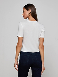 A person with long blonde hair is shown from behind, wearing the Stormy Cropped Cotton Tee in plain white and blue jeans against a light background.