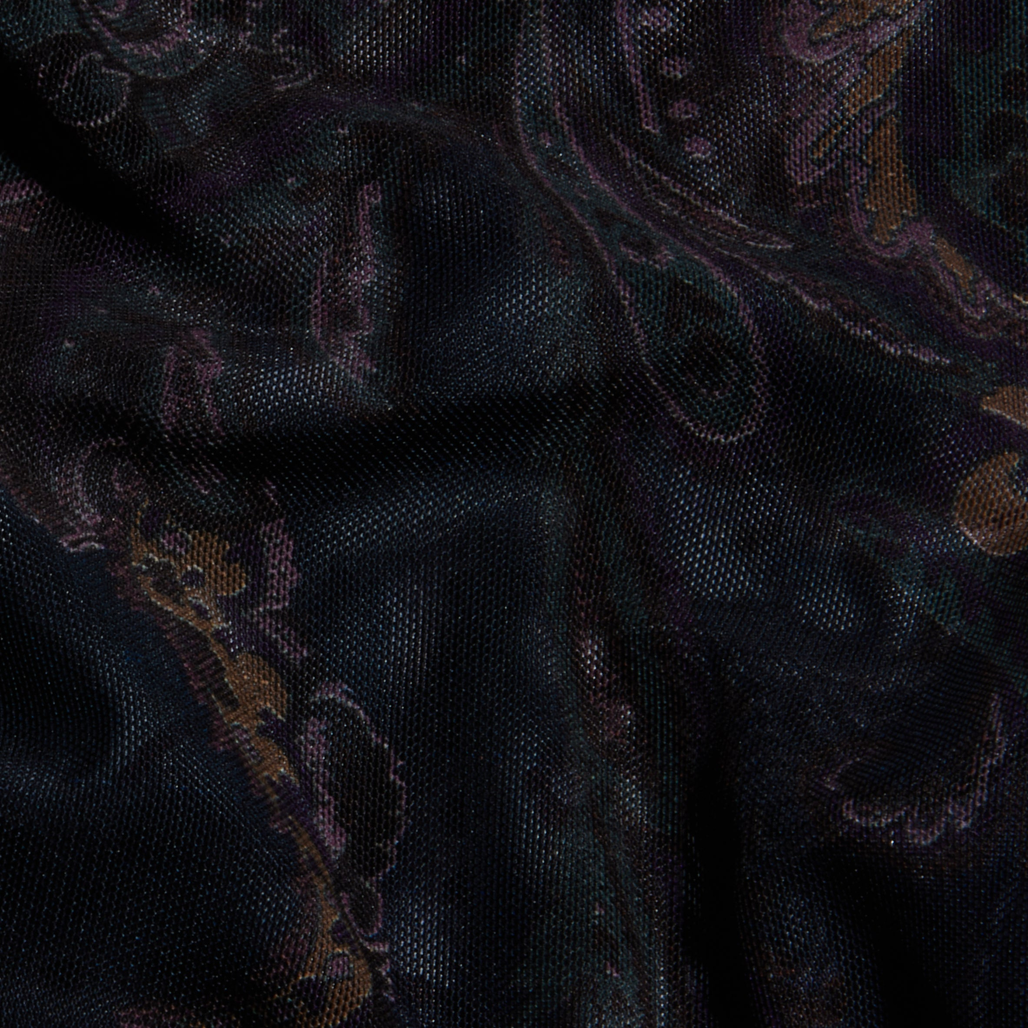Close-up of the Kalea Mesh Bodysuit, featuring dark mesh fabric adorned with a subtle midnight blue paisley pattern in muted shades of brown, green, and purple, softly illuminated to highlight the texture and delicate folds.