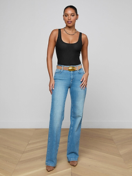 A woman wearing the Kalea Mesh Bodysuit, paired with blue high-waisted jeans and brown heels, stands against a plain white background.