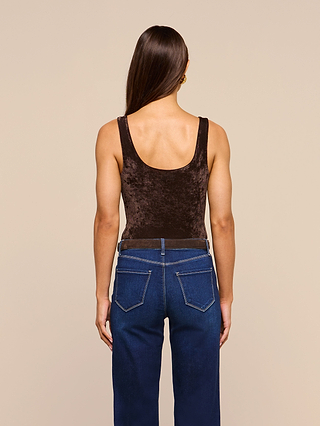 A person with long brown hair, wearing the Kalea Velvet Bodysuit—a dark brown sleeveless scoop neckline top—and blue jeans, is standing facing away from the camera against a beige background.