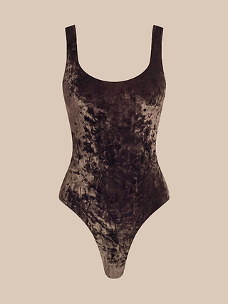 The Kalea Velvet Bodysuit, a sleeveless brown velvet piece featuring a scoop neckline and high-cut legs, is displayed against a plain beige background, making it the perfect lightweight layer for any chic wardrobe.