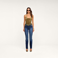 A woman stands against a beige background, wearing sunglasses, layered bracelets, tan heels, blue jeans with a double-buckle belt, and the Kalea Velvet Bodysuit in olive green featuring a stylish scoop neckline.