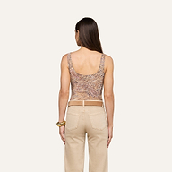 A woman with long brown hair is shown from behind, wearing the Kalea Mesh Bodysuit—a sleeveless leopard paisley print top—along with beige pants and bracelets on her left wrist, standing against a plain light background.