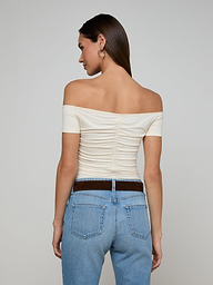 A woman is standing with her back to the camera, wearing the vintage-inspired white Baliegh Ruched Bodysuit and light blue jeans.