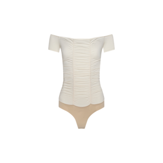 The Baliegh Ruched Bodysuit is an off-white, off-shoulder piece crafted from a rayon stretch jersey for a comfortable fit. It features allover ruching down the front, short sleeves, and an elegant off-the-shoulder neckline. The beige thong-style bottom and form-fitting silhouette create a sleek look, showcased here against a plain white background.