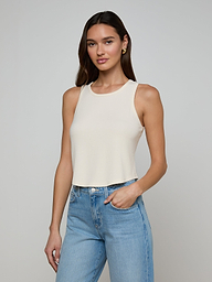 A woman wearing the Cael Tank Top in white and light blue jeans stands against a plain light background, one hand in her pocket and a slight smile.