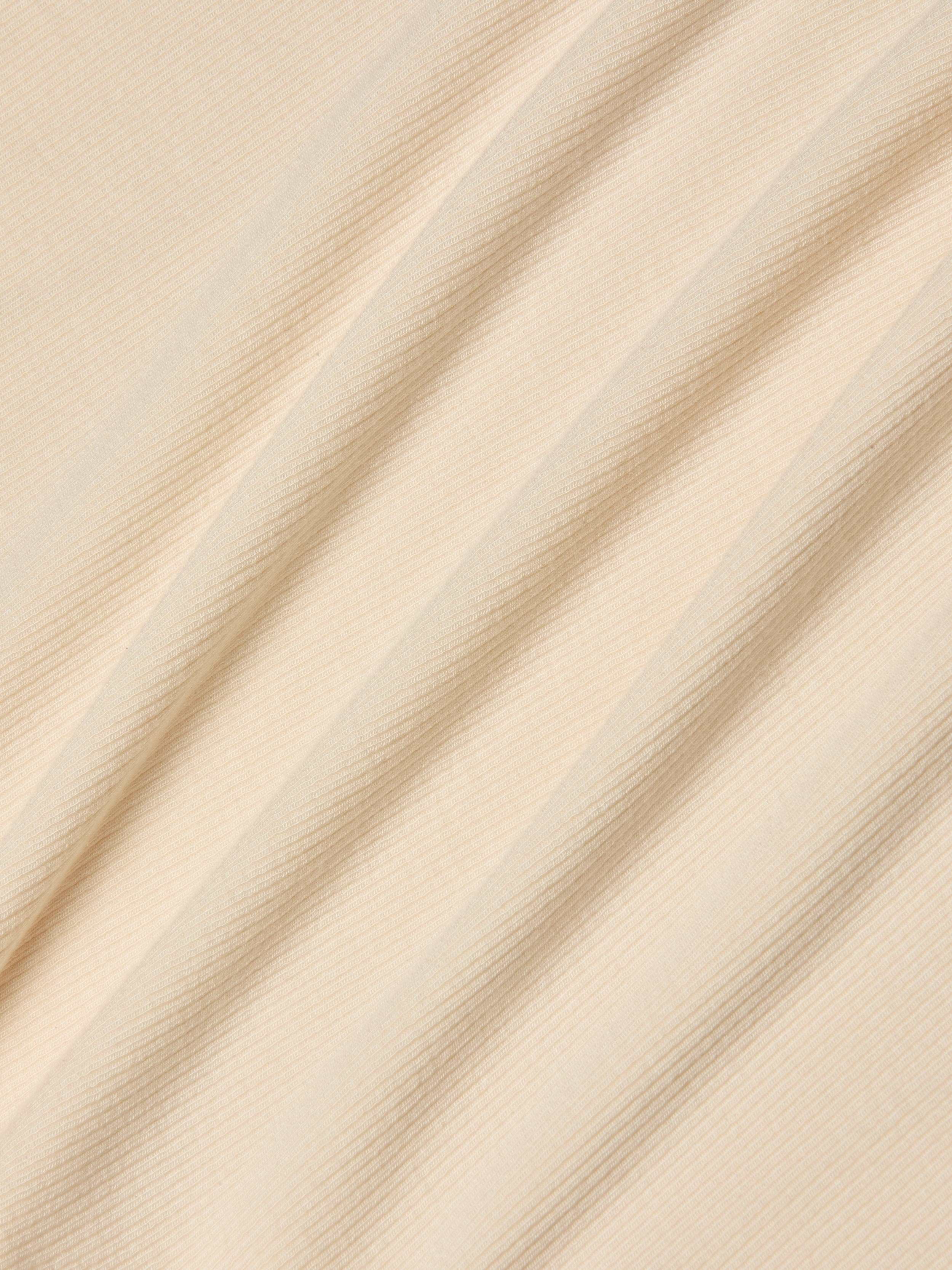 Beige ribbed fabric with diagonal folds, showcasing a subtle striped texture under soft, even lighting. Perfect for the Cael Tank Top, the material appears smooth, lightweight, and ultra soft—ideal for layering or wearing on its own.