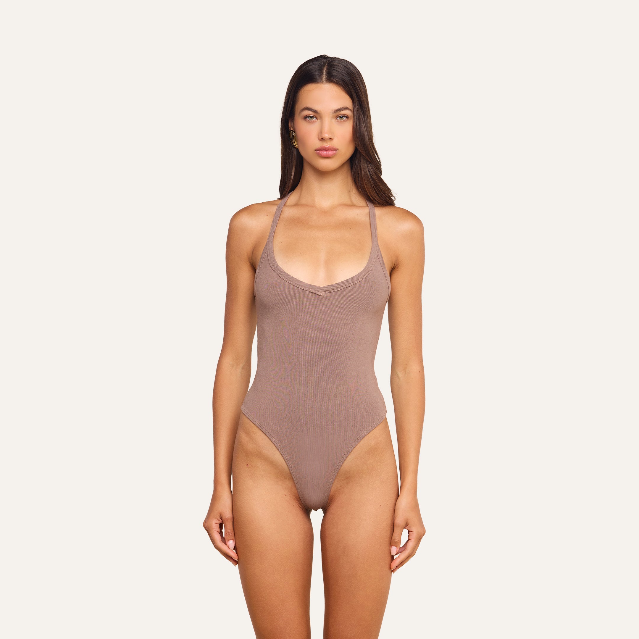 A woman stands facing forward against a plain light background, wearing the Wrenna Racerback Bodysuit in taupe rib fabric.