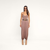 A woman wearing sunglasses, the Wrenna Racerback Bodysuit in taupe rib fabric, loose mauve pants with a belt, and beige boots stands against a plain white background.