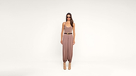 Woman in sunglasses wearing a tan jumpsuit with a brown belt and ankle boots stands against a plain white background.