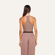 A woman stands facing away from the camera, wearing the Wrenna Racerback Bodysuit in taupe-colored ribbed fabric paired with matching high-waisted pants against a plain light background.