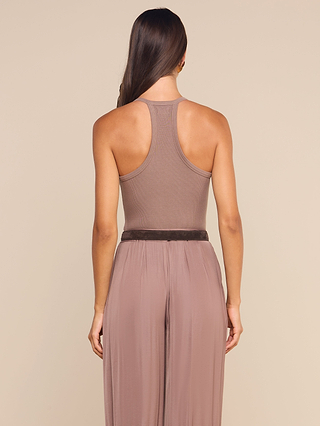 A person with long brown hair, wearing the Wrenna Racerback Bodysuit in mauve rib fabric and matching wide-leg pants, stands with their back to the camera against a plain beige background.