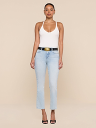A woman stands against a beige background, wearing the Wrenna Racerback Bodysuit in white rib fabric, light blue high-waisted jeans, a black belt with a gold buckle, and black open-toe heels. She faces forward with arms at her sides.