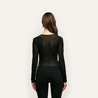 A person seen from behind wearing a black long-sleeve Thalassa Velvet Mesh Bodysuit tucked into black jeans with a belt.