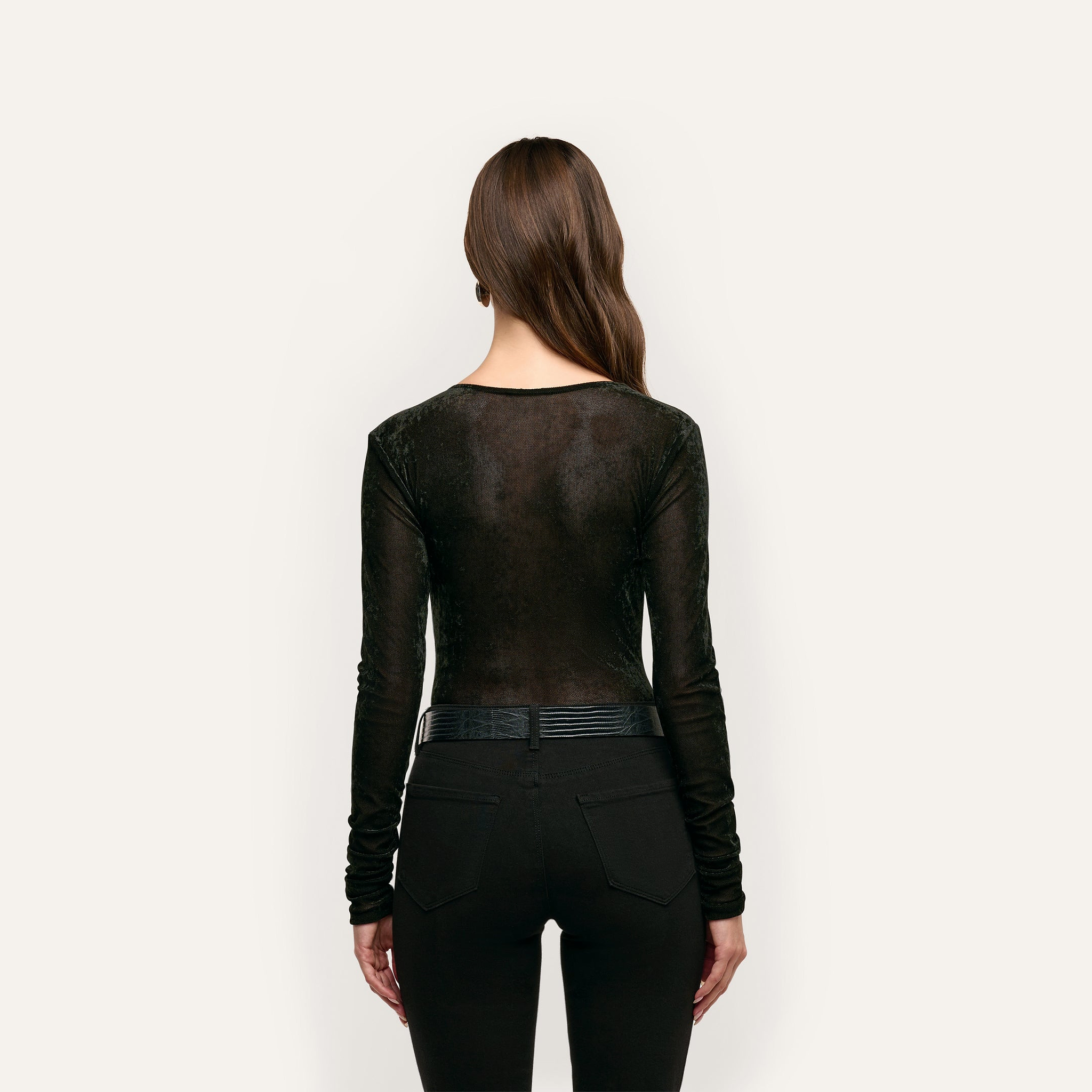 A person seen from behind wearing a black long-sleeve Thalassa Velvet Mesh Bodysuit tucked into black jeans with a belt.