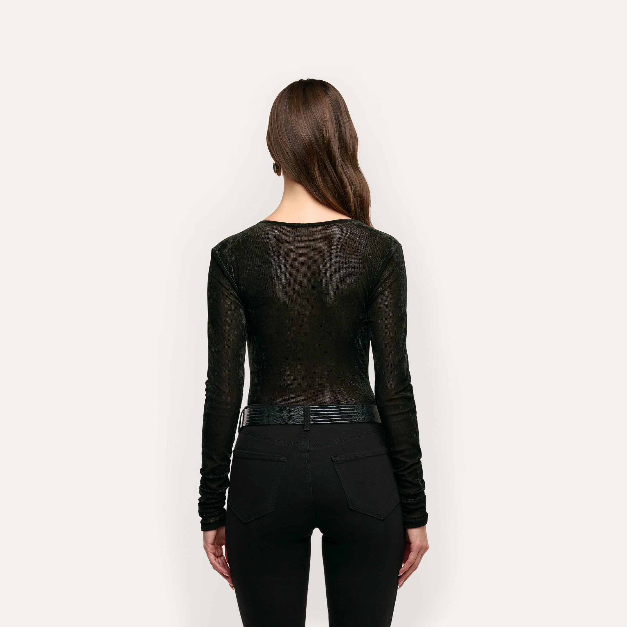 A person seen from behind wearing a black long-sleeve Thalassa Velvet Mesh Bodysuit tucked into black jeans with a belt.