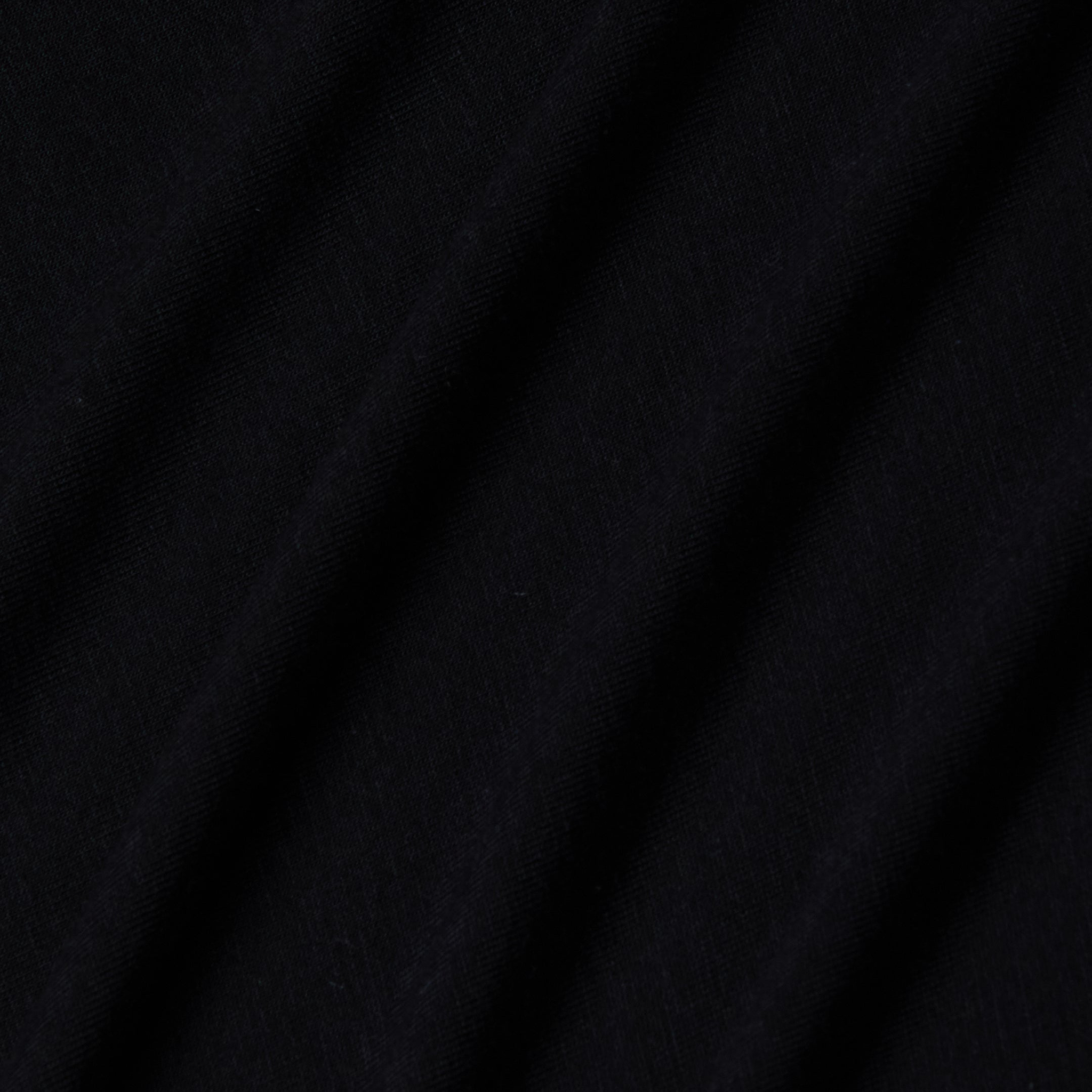 Close-up of black stretch jersey fabric with soft, diagonal folds creating gentle shadows and texture, highlighting the smooth and slightly matte surface characteristic of the Riza Boatneck Bodysuit.