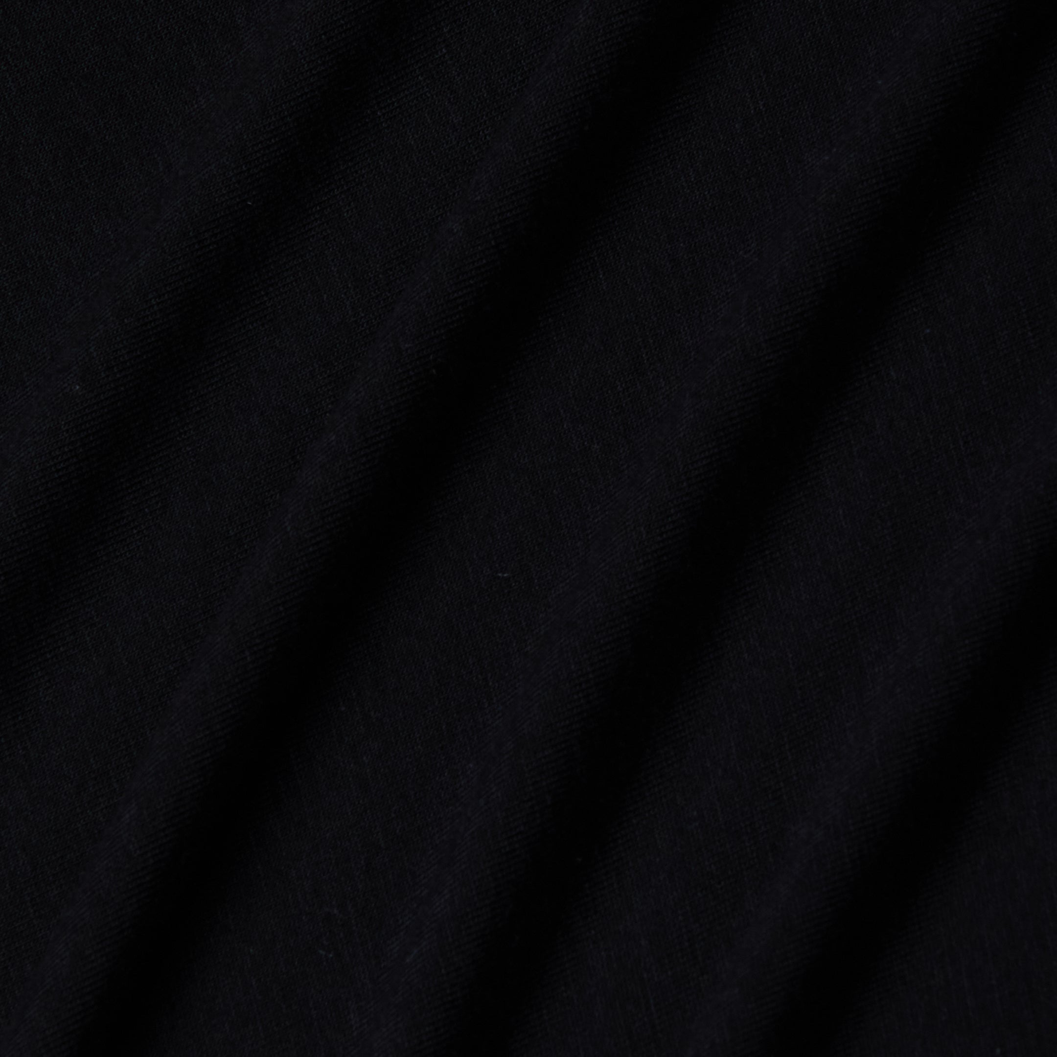 Close-up of black stretch jersey fabric with soft, diagonal folds creating gentle shadows and texture, highlighting the smooth and slightly matte surface characteristic of the Riza Boatneck Bodysuit.