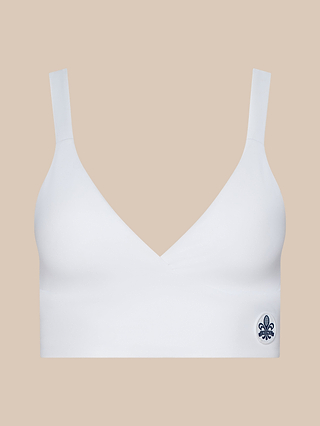 Steffi Tennis Bralette featuring wide shoulder straps and a deep V-neckline, crafted from moisture-wicking sports fabric with a small dark blue fleur-de-lis emblem on the lower left side, displayed against a plain beige background.