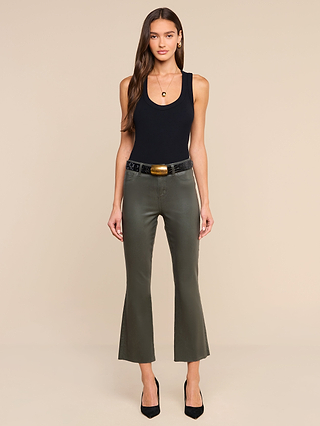 Woman stands facing forward, wearing the Shania Racerback Tank in black, paired with olive-green flared pants, a black belt with a gold buckle, and black heels, against a plain beige background.