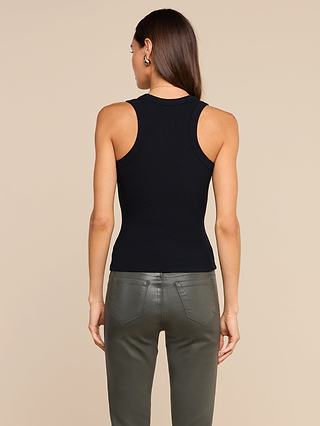 A woman stands facing away, wearing the Shania Racerback Tank in black and dark green leather pants. Her straight brown hair is down, and she is set against a plain beige background.