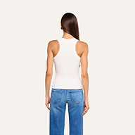 Una persona dai lunghi capelli castani, che indossa la canotta Shania Racerback in bianco e dei jeans blu, è in piedi di spalle alla fotocamera su uno sfondo beige a tinta unita.