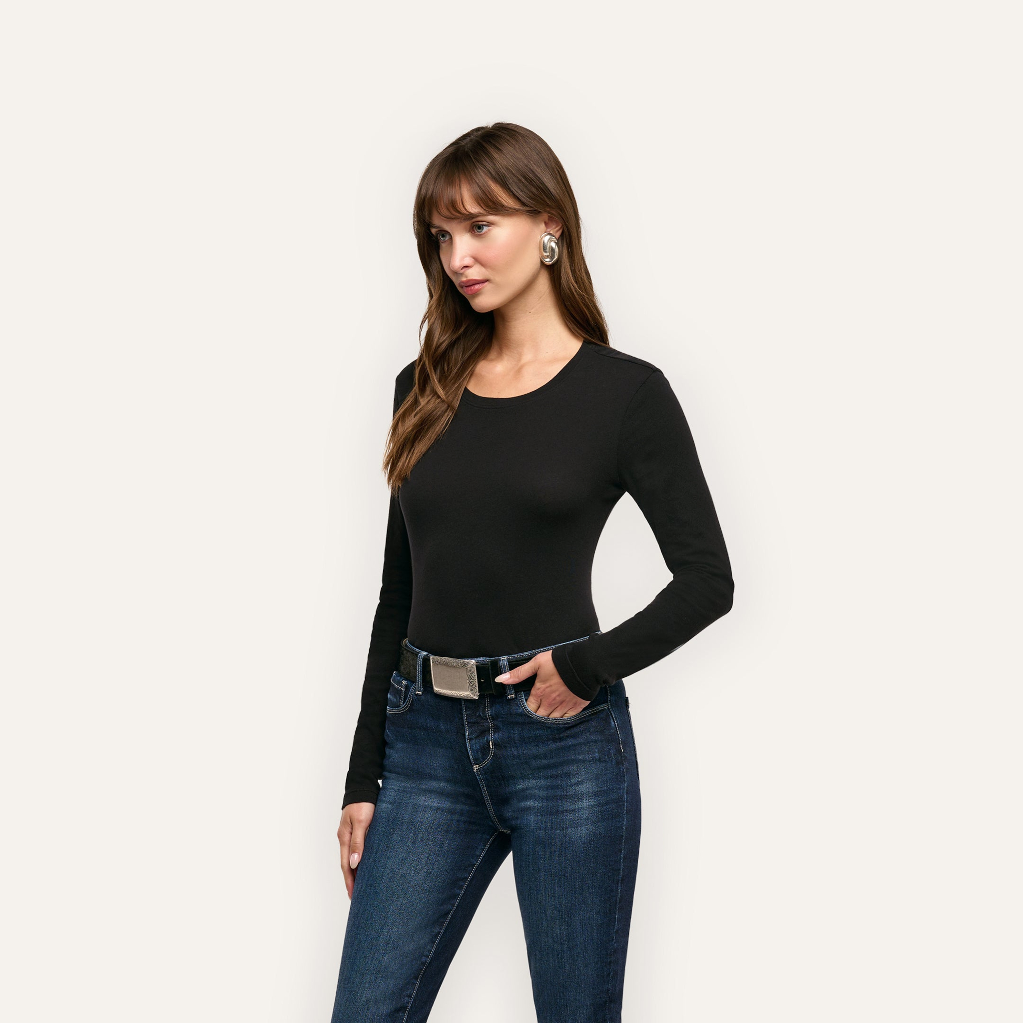 A woman wearing a black long-sleeved Leanne Cotton Tee tucked into dark blue jeans with a silver-buckled belt.