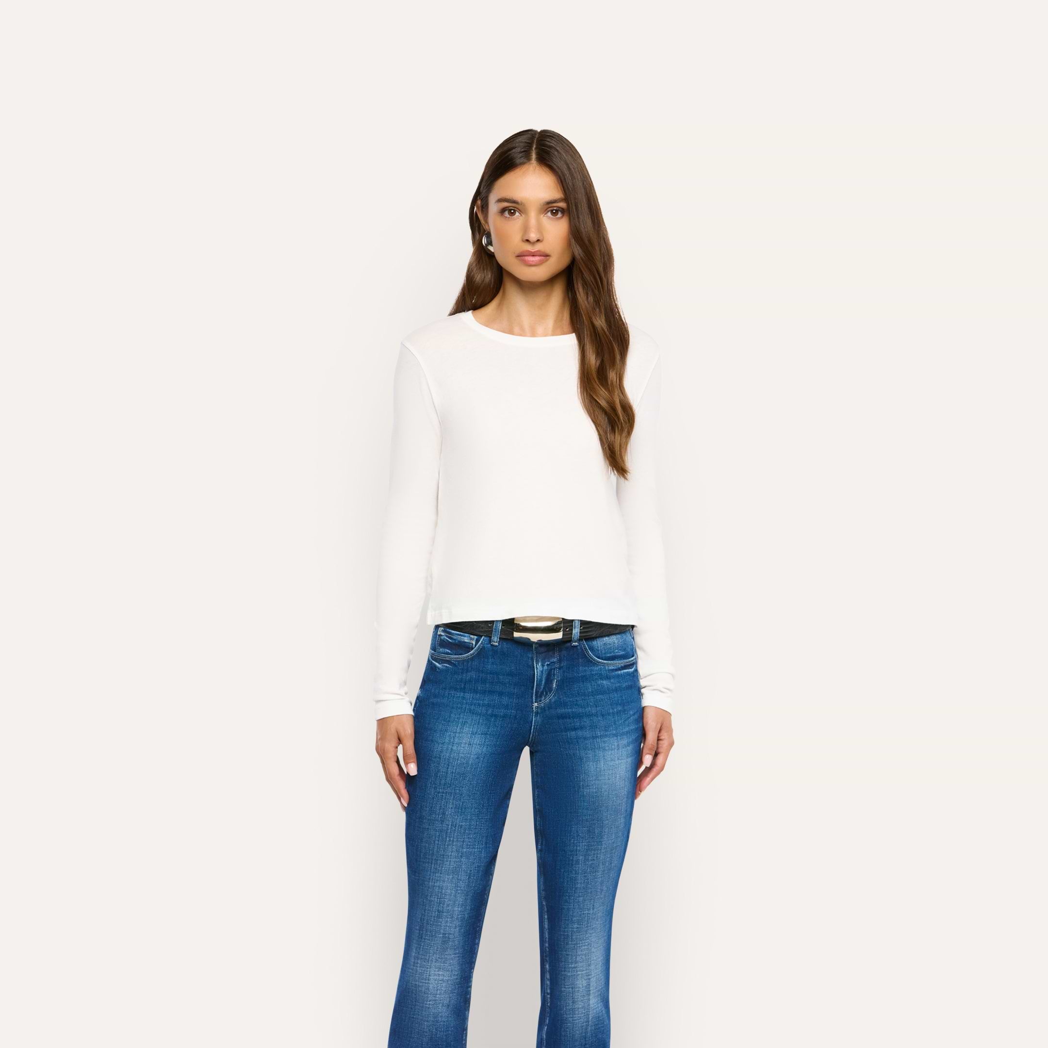 A woman wearing a white long-sleeved Leanne Cotton Tee and blue jeans with a black belt.