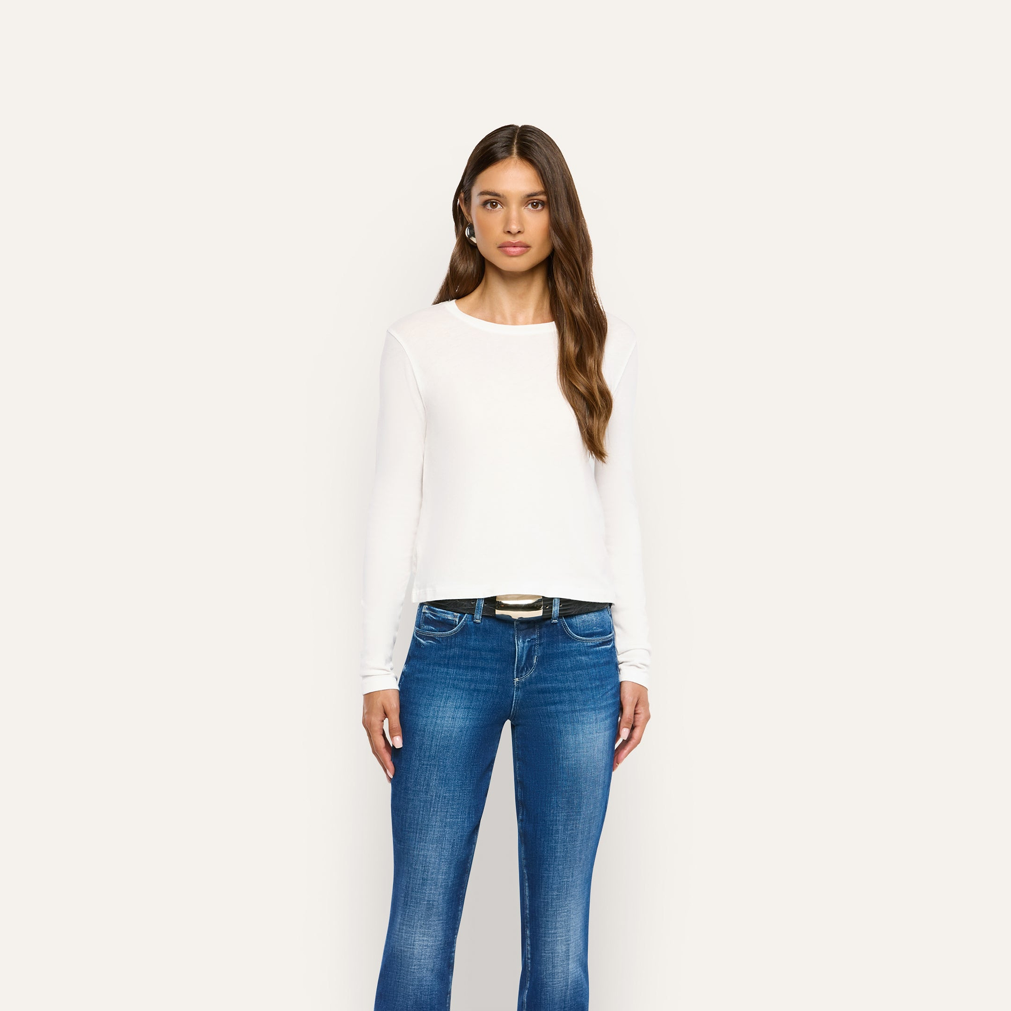 A woman wearing a white long-sleeved Leanne Cotton Tee and blue jeans with a black belt.