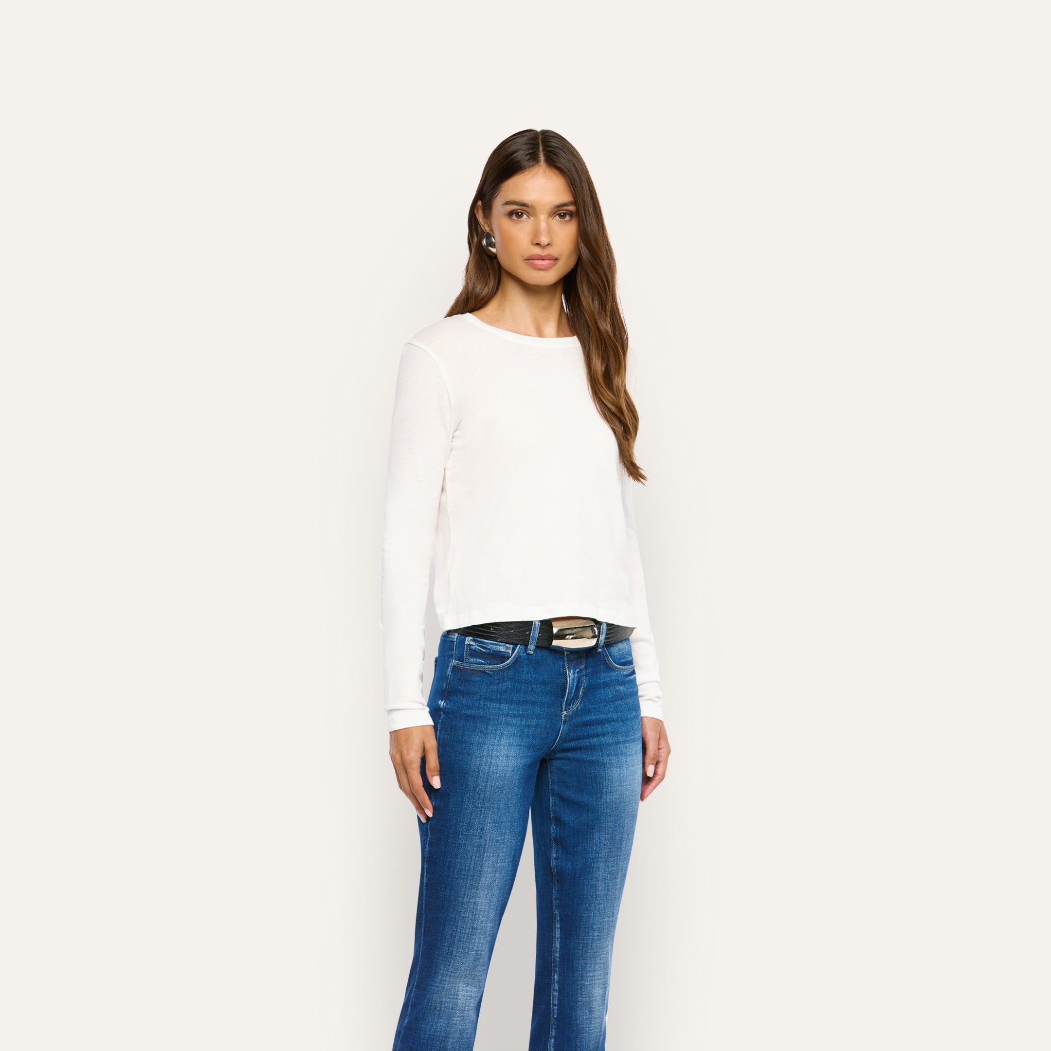 A woman wearing a white Leanne Cotton Tee tucked into blue jeans with a black belt.