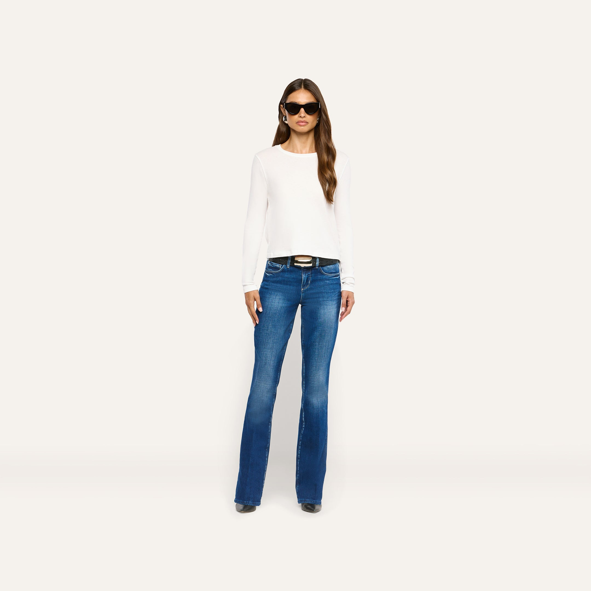 A person wearing a white Leanne Cotton Tee, a black belt, and blue flared jeans.