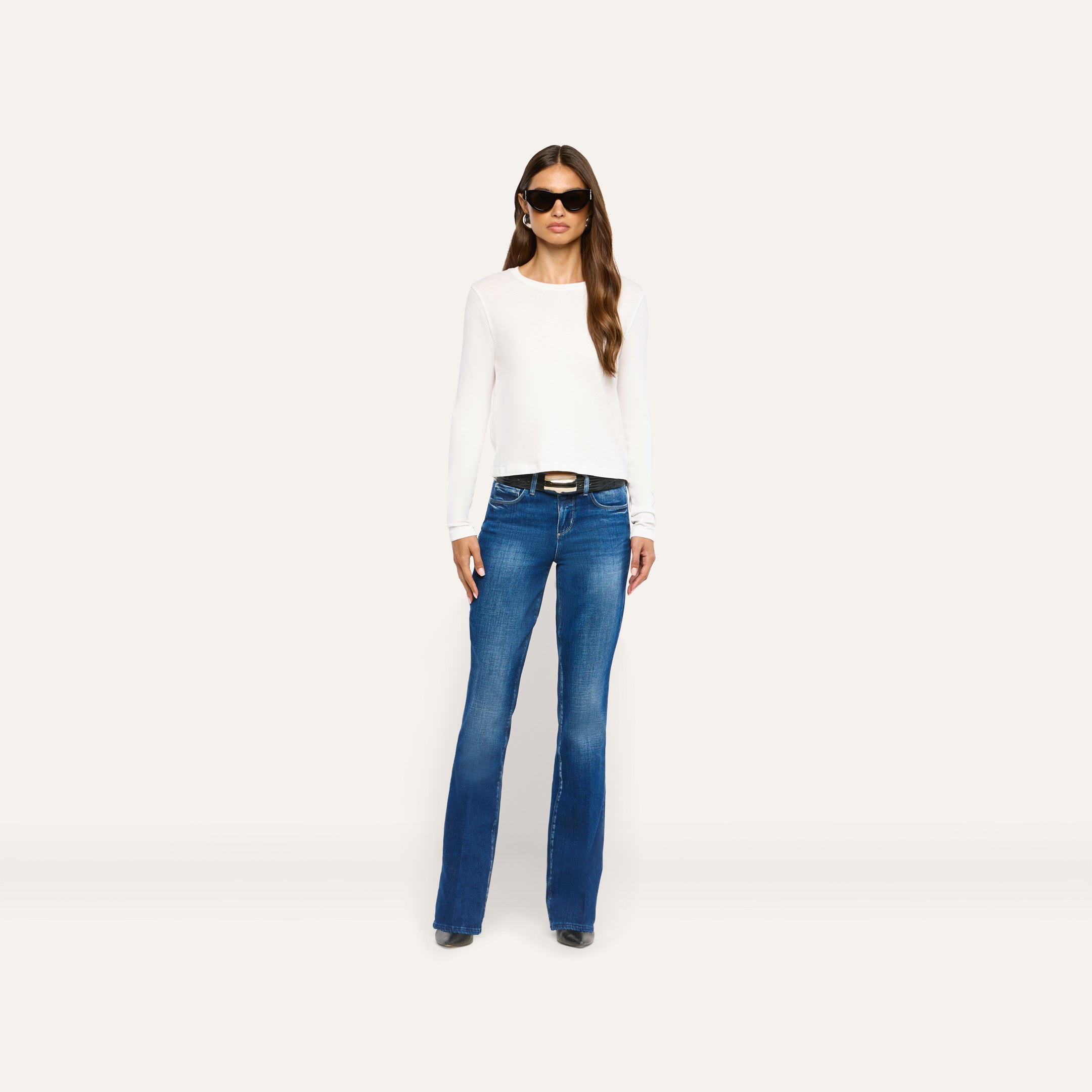 A person wearing a white Leanne Cotton Tee, a black belt, and blue flared jeans.