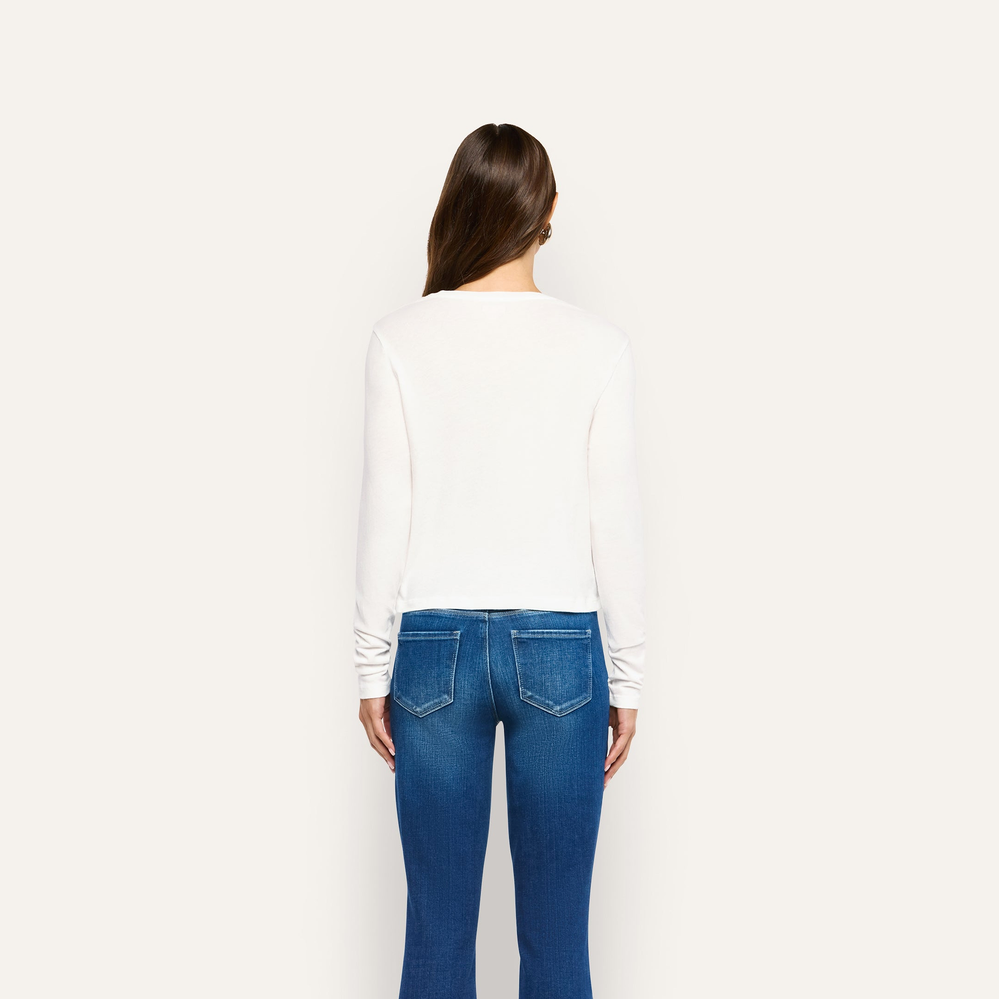 A person seen from behind, wearing a long-sleeved white Leanne Cotton Tee and blue jeans.