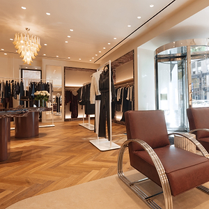 Luxury clothing store interior with brown leather chairs and wooden flooring.