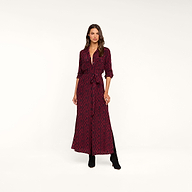 A woman stands against a plain beige background wearing the Cameron Silk Shirt Dress, a long-sleeve, button-down style in maroon with a black geometric pattern, cinched at the waist and paired with black boots.