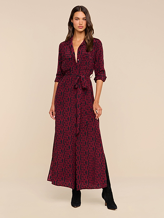 A woman stands against a plain beige background wearing the Cameron Silk Shirt Dress, a long-sleeve, button-down style in maroon with a black geometric pattern, cinched at the waist and paired with black boots.