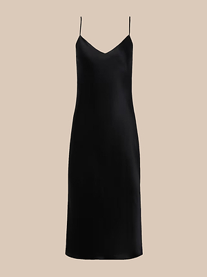 The Jodie Silk Slip Dress is a simple black slip dress with a smooth, silky texture, V-neckline, and adjustable spaghetti straps. Bias cut and knee length, it’s showcased on a plain beige background.