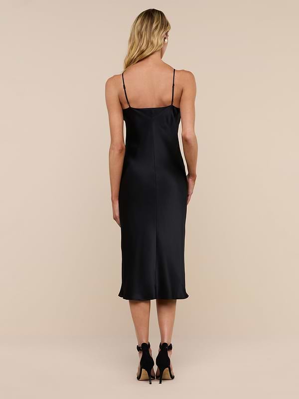 Wearing the Jodie Silk Slip Dress and black high heels, a woman with long blonde hair stands facing away from the camera against a plain white background.
