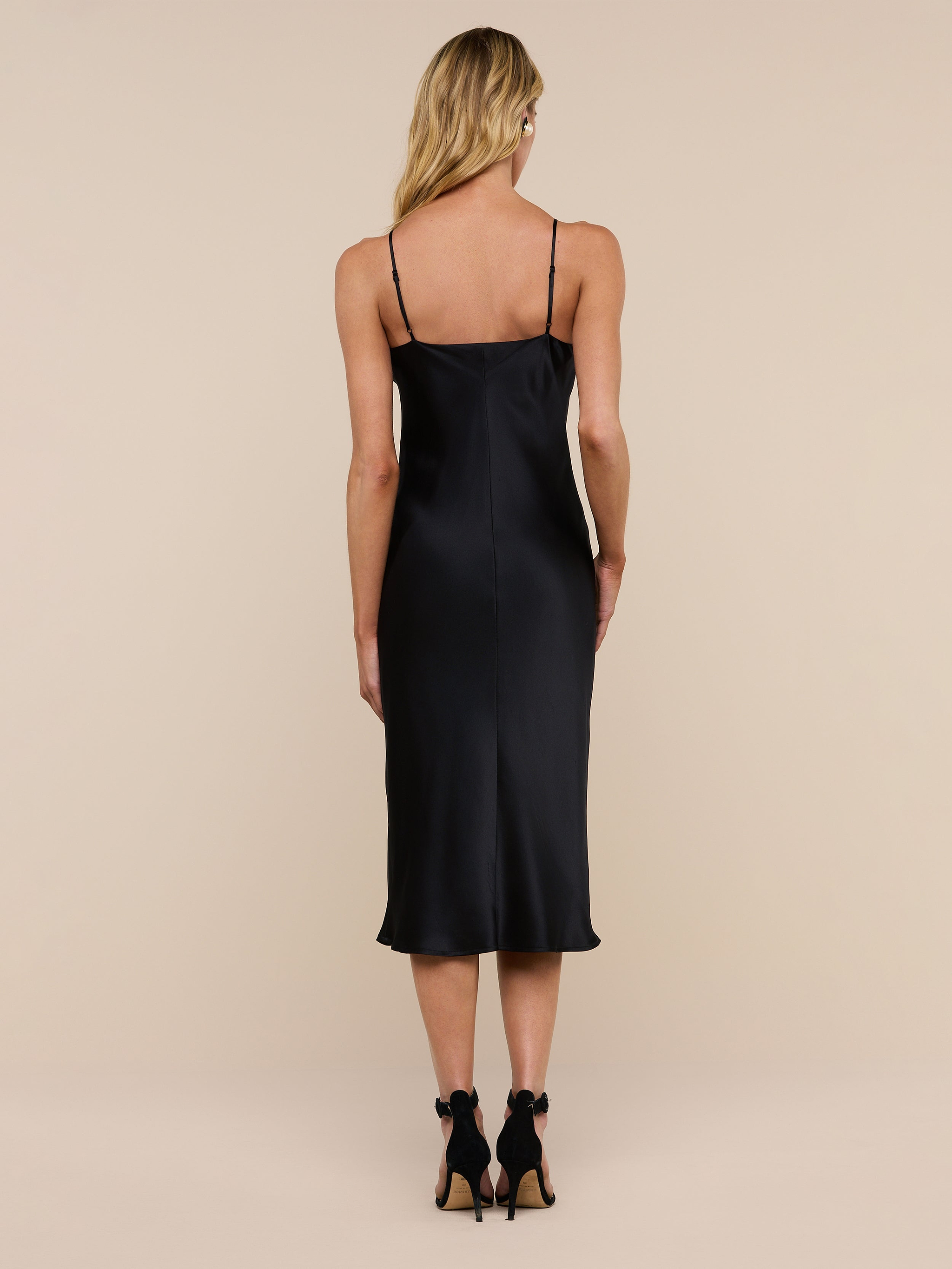 Wearing the Jodie Silk Slip Dress and black high heels, a woman with long blonde hair stands facing away from the camera against a plain white background.