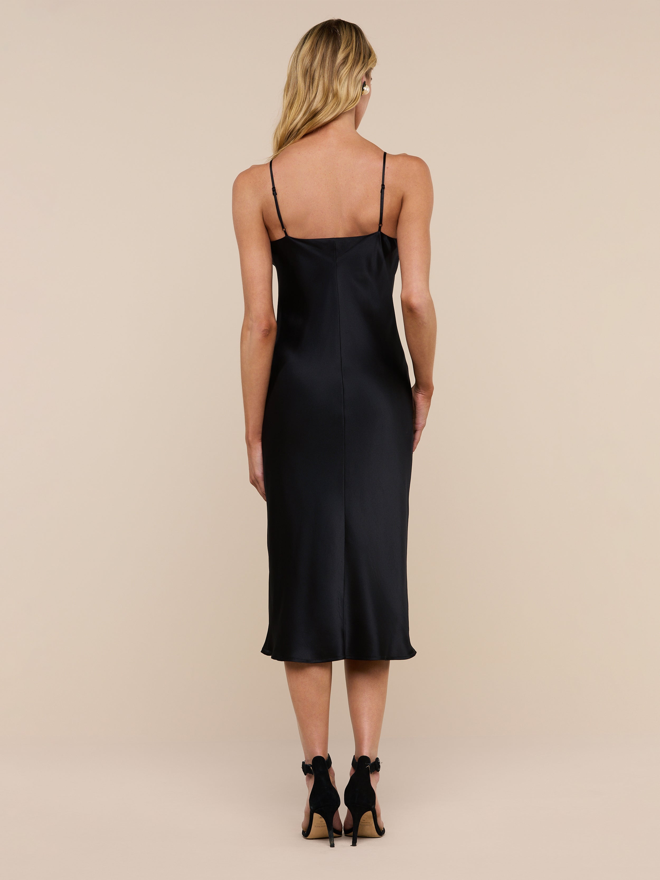 Wearing the Jodie Silk Slip Dress and black high heels, a woman with long blonde hair stands facing away from the camera against a plain white background.