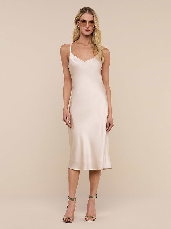 A woman stands facing forward against a plain white background wearing the Jodie Silk Slip Dress in champagne with spaghetti straps, paired with strappy high-heeled sandals.